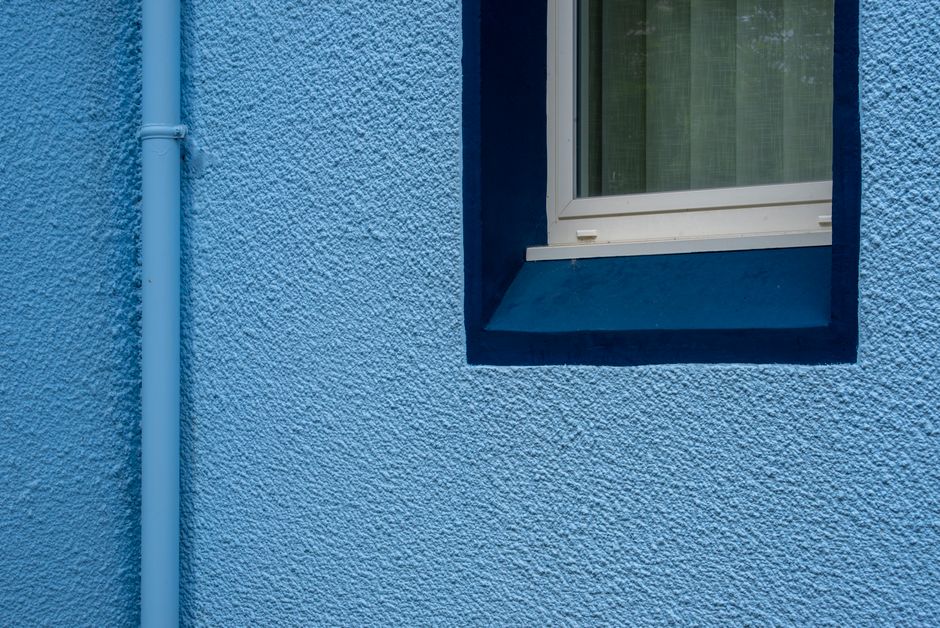 A painted blue wall with a window and a drainpipe.