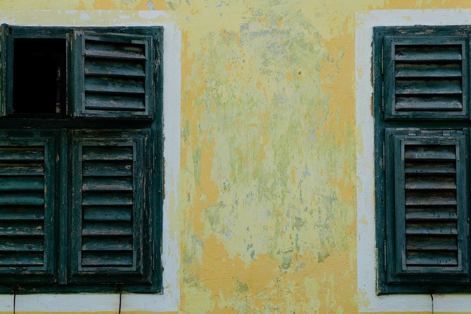 Wooden louvered shutters on a faded yellow painted wall.