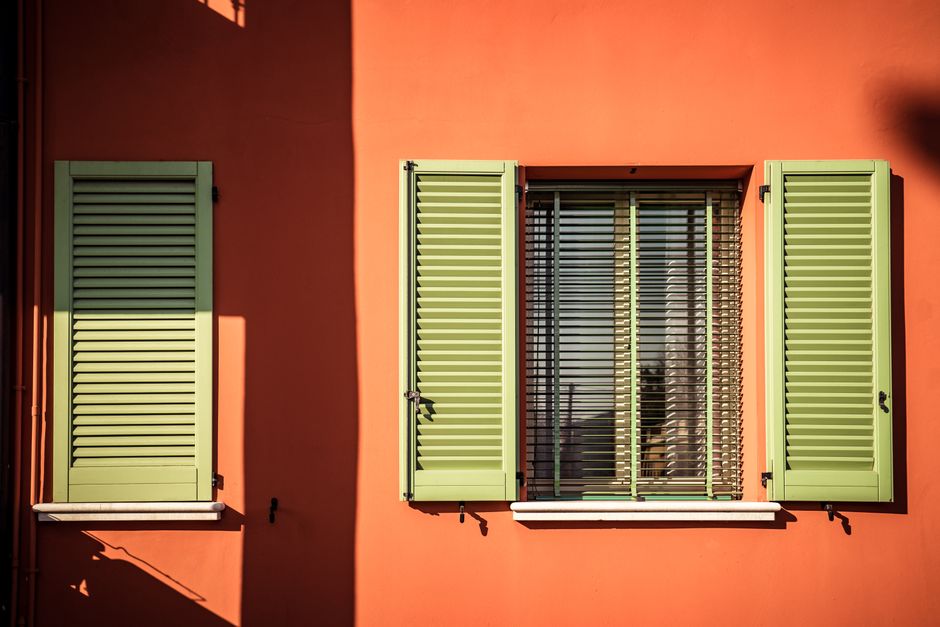 An orange painted wall with green shutters.