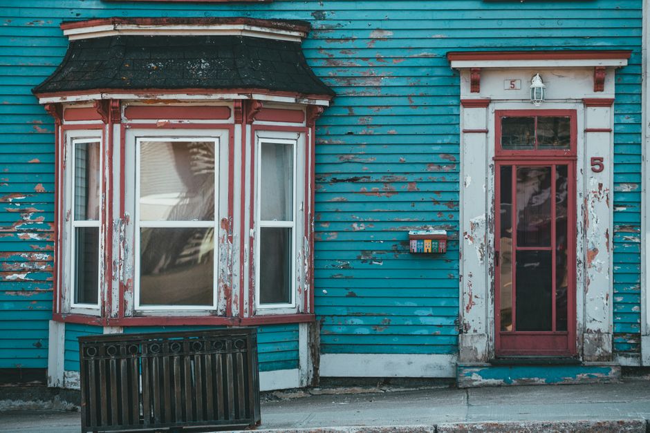 A weathered blue painted wall with a bay window and a door.