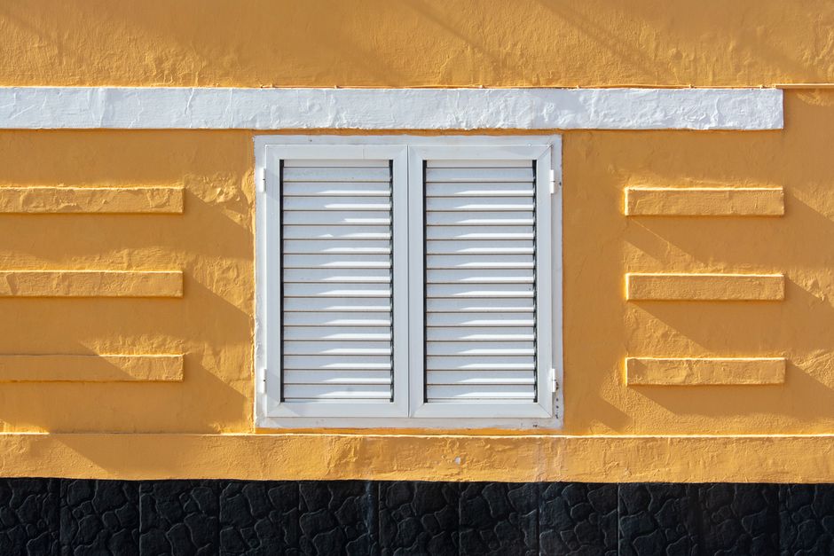 A yellow painted wall with white shutters.