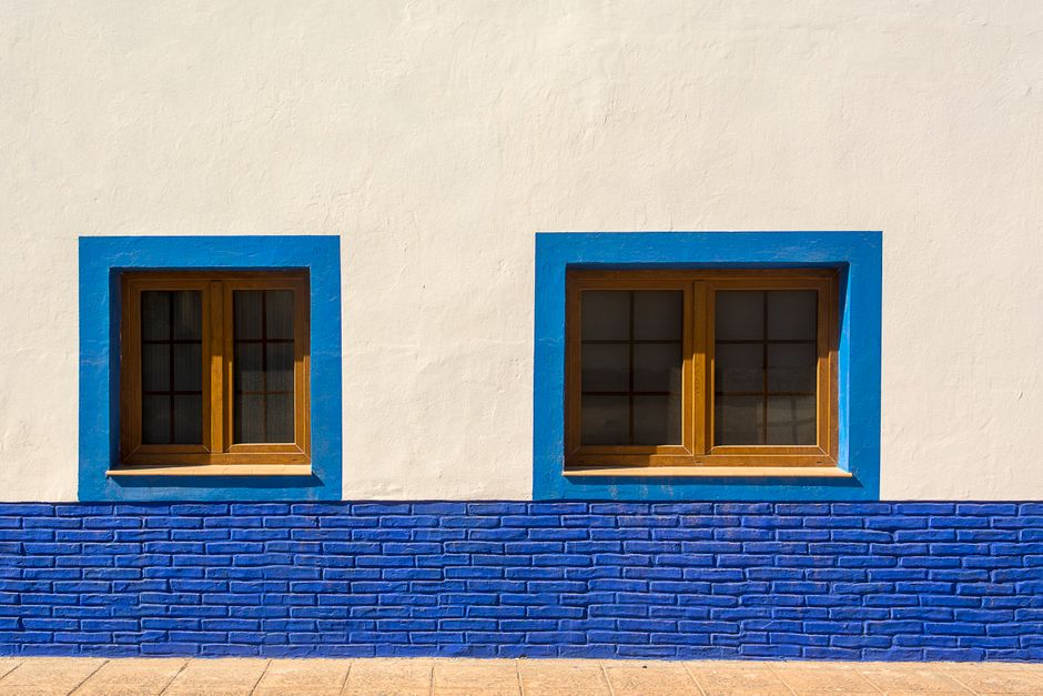 Blue framed windows on a white painted wall in sunlight.