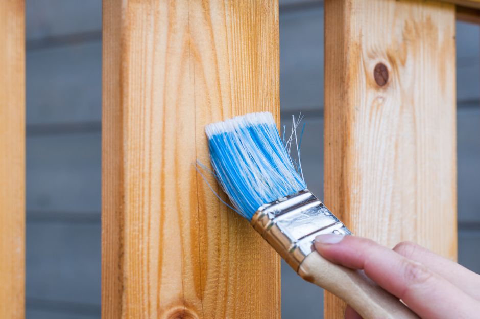 A hand painting a wooden plank with a blue paintbrush outdoors.